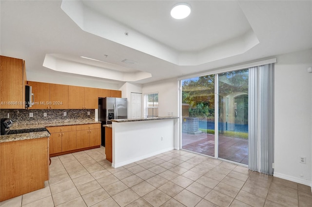 kitchen with stone countertops, stainless steel appliances, light tile patterned floors, and a raised ceiling