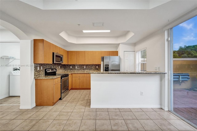 kitchen featuring stainless steel appliances, stone countertops, light tile patterned flooring, washer / clothes dryer, and decorative backsplash