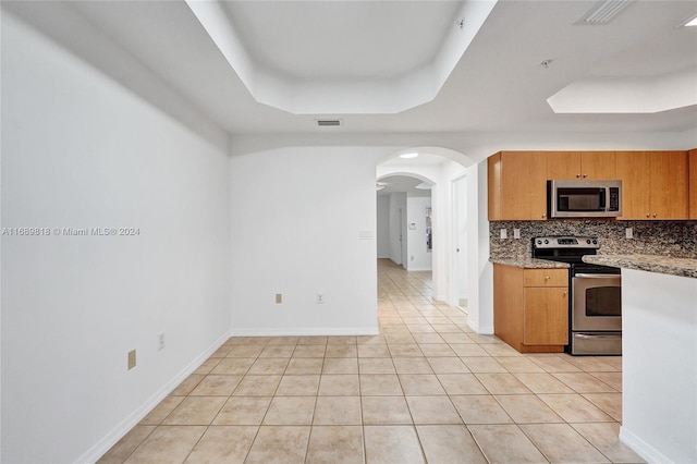 kitchen featuring light stone counters, light tile patterned flooring, backsplash, appliances with stainless steel finishes, and a raised ceiling