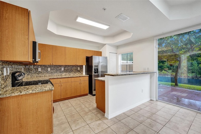 kitchen featuring stainless steel appliances, kitchen peninsula, light stone countertops, a raised ceiling, and decorative backsplash