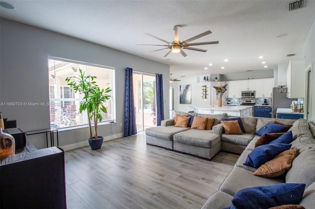 living room with light wood-type flooring, a textured ceiling, and ceiling fan