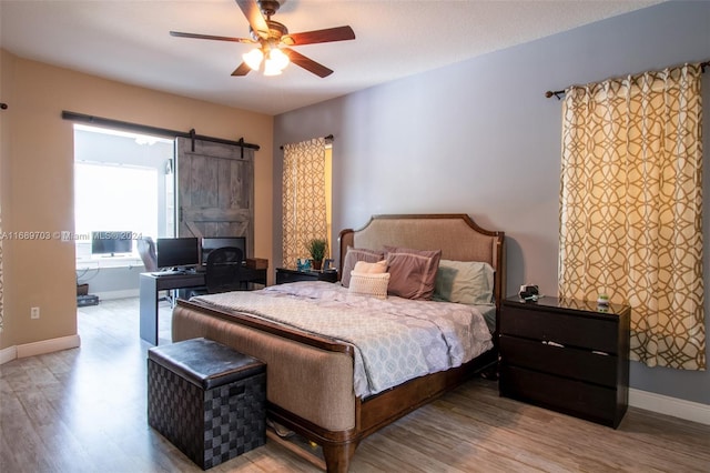 bedroom with a barn door, ceiling fan, and light hardwood / wood-style flooring