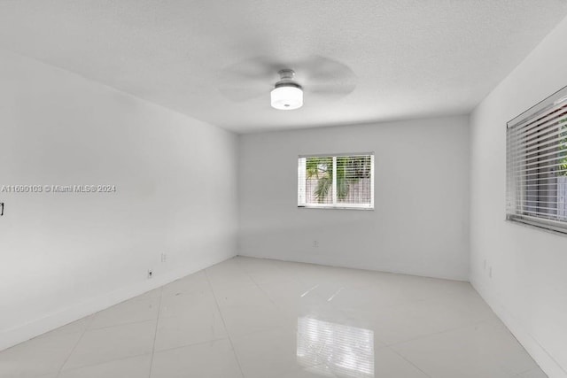 unfurnished room with ceiling fan, light tile patterned flooring, and a textured ceiling