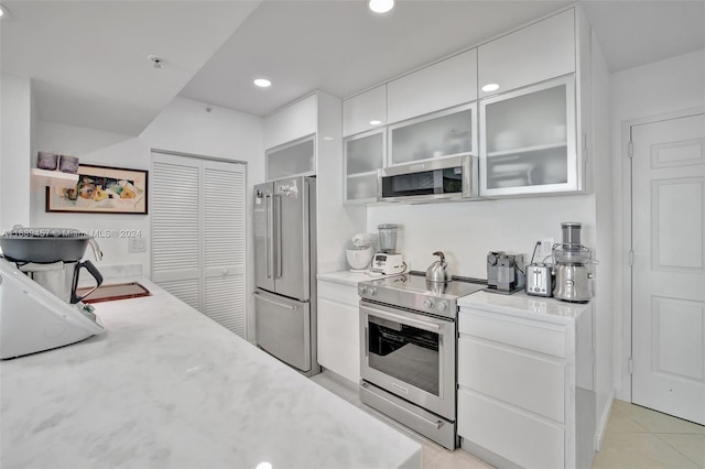 kitchen with appliances with stainless steel finishes, light tile patterned flooring, and white cabinets