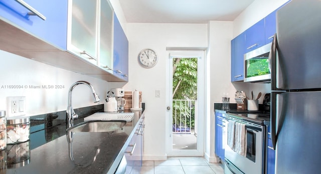 kitchen featuring stainless steel appliances, sink, light tile patterned floors, blue cabinetry, and dark stone countertops