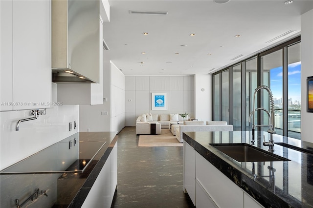 kitchen featuring dark stone countertops, sink, a wall of windows, and white cabinets