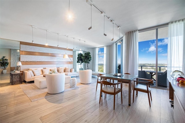 dining space featuring light wood-type flooring, rail lighting, and a wall of windows