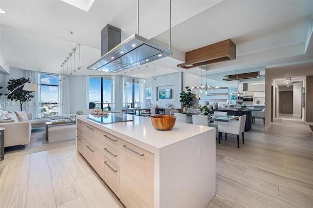 kitchen featuring a center island, decorative light fixtures, black electric cooktop, light brown cabinetry, and light wood-type flooring