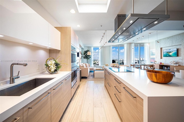 kitchen featuring black electric cooktop, double oven, sink, light brown cabinets, and light hardwood / wood-style floors