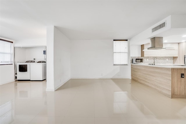 kitchen featuring light tile patterned flooring, light brown cabinets, decorative backsplash, independent washer and dryer, and wall chimney exhaust hood