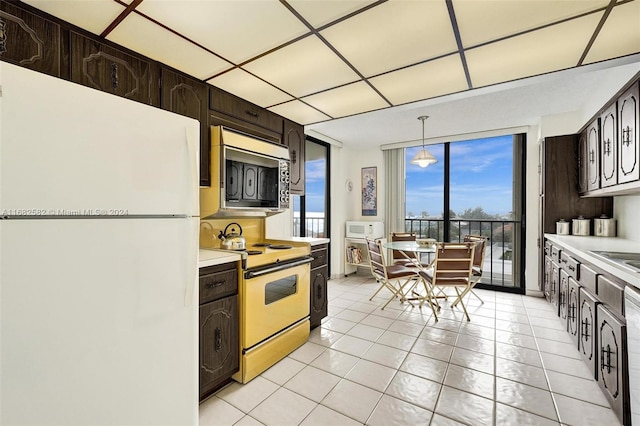 kitchen featuring dark brown cabinetry, white appliances, decorative light fixtures, and light tile patterned flooring