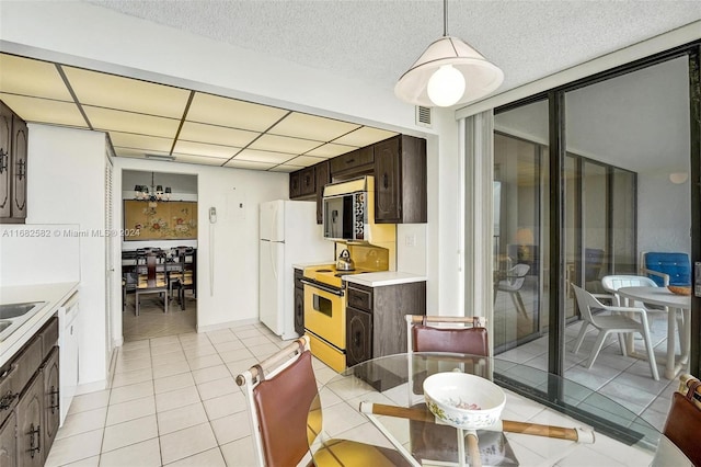 kitchen featuring dark brown cabinetry, white appliances, light tile patterned floors, and decorative light fixtures