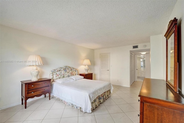 bedroom with ensuite bathroom, a textured ceiling, light tile patterned floors, and a closet