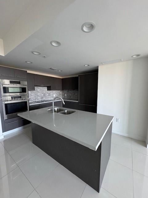 kitchen featuring decorative backsplash, light tile patterned floors, a kitchen island with sink, and sink