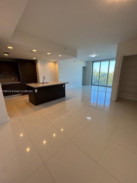 kitchen with expansive windows, sink, light tile patterned floors, and an island with sink