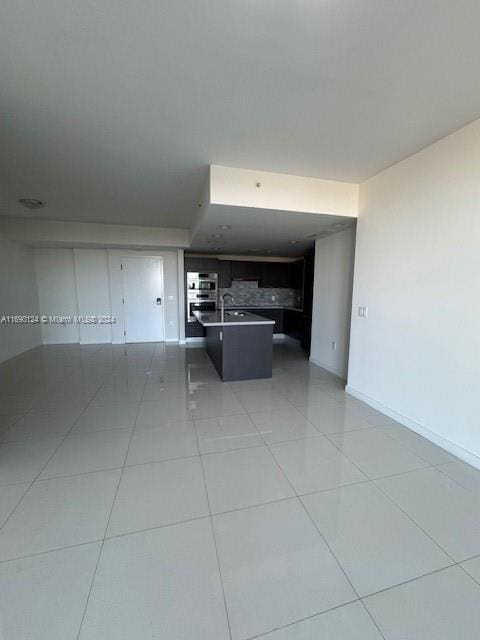 kitchen with backsplash, a kitchen island with sink, sink, light tile patterned floors, and stainless steel double oven