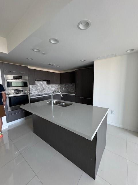 kitchen featuring decorative backsplash, sink, light tile patterned floors, and a kitchen island with sink