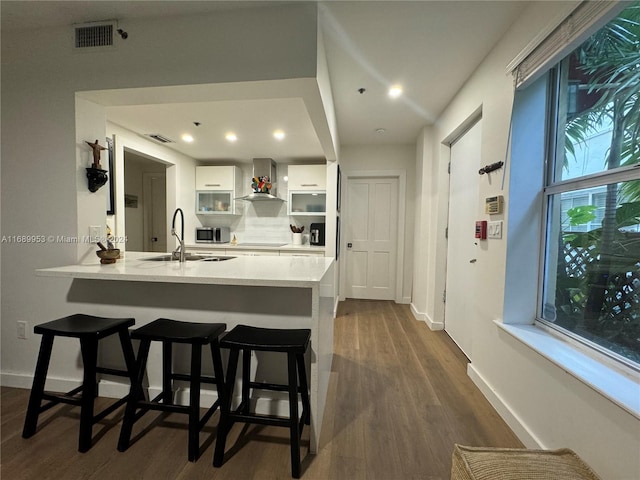 kitchen featuring white cabinetry, sink, dark wood-type flooring, kitchen peninsula, and wall chimney exhaust hood