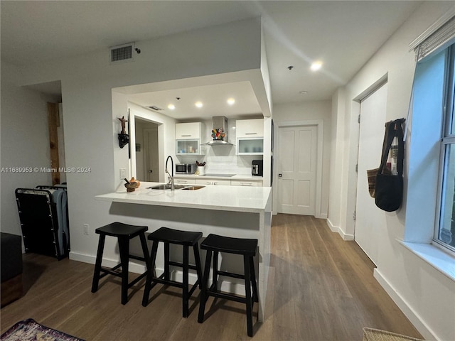 kitchen with white cabinetry, sink, a breakfast bar area, dark wood-type flooring, and wall chimney range hood