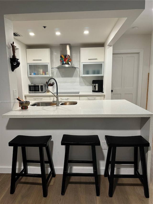 kitchen with white cabinets, wall chimney range hood, dark hardwood / wood-style floors, and a breakfast bar area