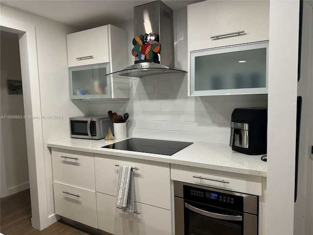 kitchen featuring dark hardwood / wood-style flooring, white cabinets, tasteful backsplash, wall chimney range hood, and appliances with stainless steel finishes