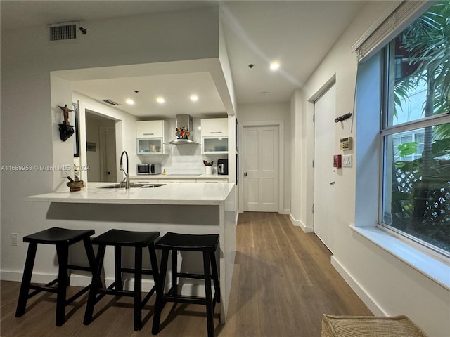 kitchen featuring sink, a kitchen bar, wall chimney exhaust hood, white cabinets, and dark wood-type flooring