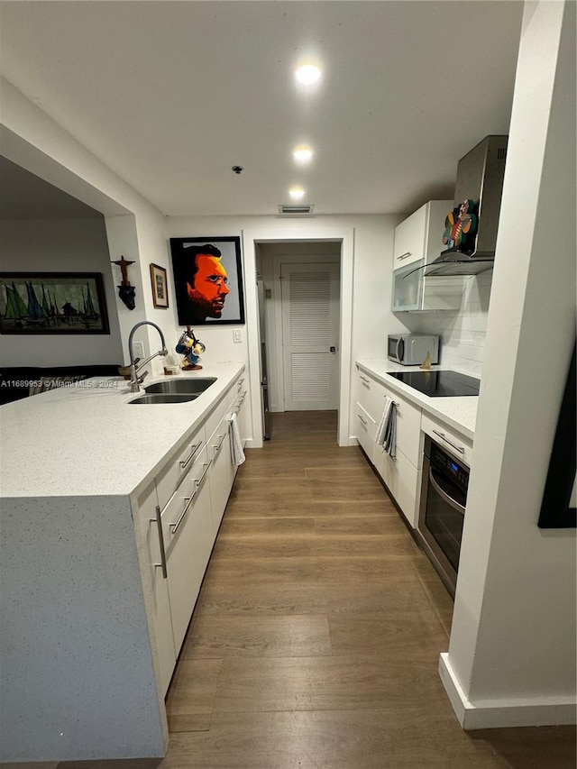 kitchen with wood-type flooring, appliances with stainless steel finishes, sink, white cabinets, and kitchen peninsula