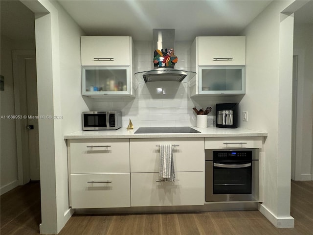 kitchen with white cabinets, appliances with stainless steel finishes, dark wood-type flooring, and wall chimney range hood