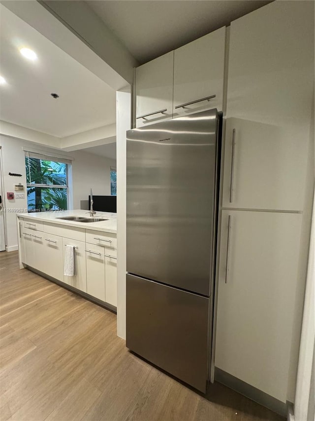 kitchen with light hardwood / wood-style floors, sink, stainless steel fridge, and white cabinets