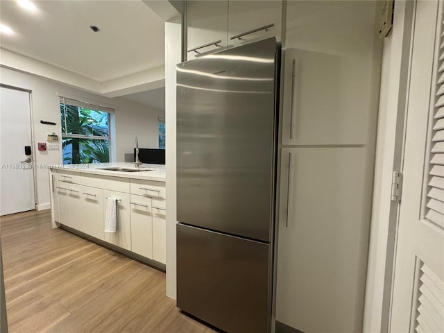 kitchen featuring white cabinets, light hardwood / wood-style floors, stainless steel fridge, and sink