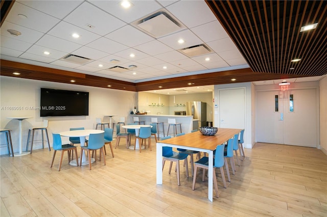 dining area with a drop ceiling, light wood-type flooring, and visible vents