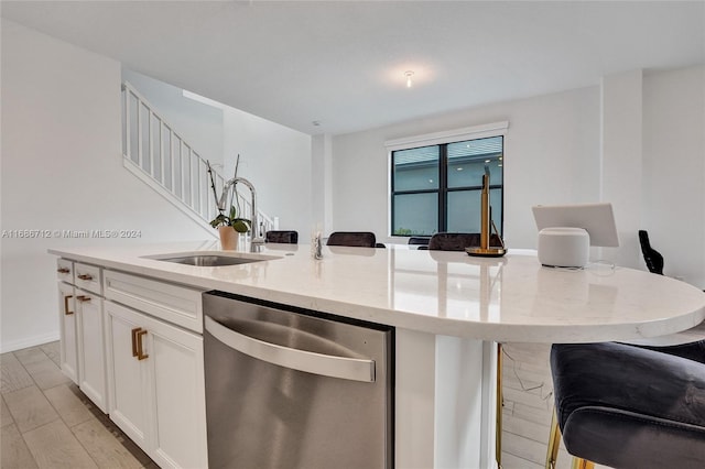 kitchen featuring white cabinetry, light hardwood / wood-style flooring, stainless steel dishwasher, and an island with sink