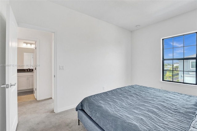 bedroom featuring light colored carpet, ensuite bath, and sink