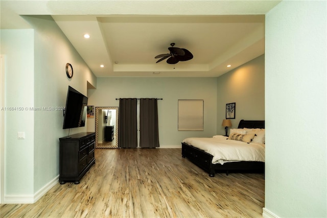 bedroom with ceiling fan, light hardwood / wood-style floors, and a raised ceiling