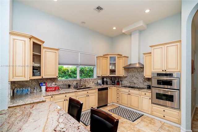 kitchen with decorative backsplash, wall chimney exhaust hood, sink, light stone countertops, and appliances with stainless steel finishes