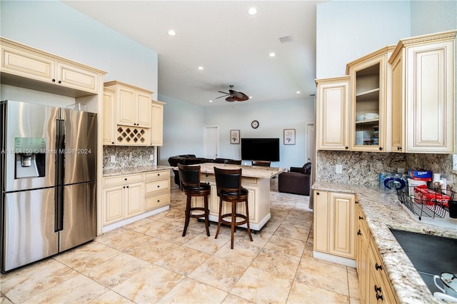 kitchen with stainless steel fridge with ice dispenser, a kitchen breakfast bar, ceiling fan, light stone countertops, and cream cabinetry