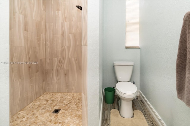 bathroom with wood-type flooring, toilet, and a tile shower