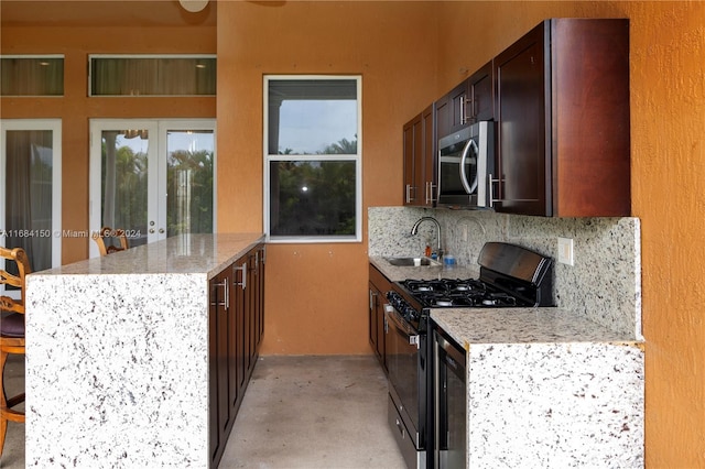 kitchen featuring sink, kitchen peninsula, light stone counters, appliances with stainless steel finishes, and tasteful backsplash