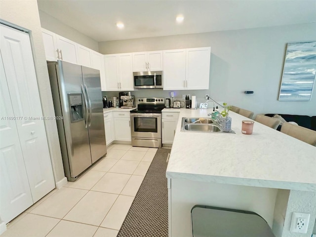 kitchen featuring stainless steel appliances, white cabinets, kitchen peninsula, light tile patterned floors, and a kitchen breakfast bar