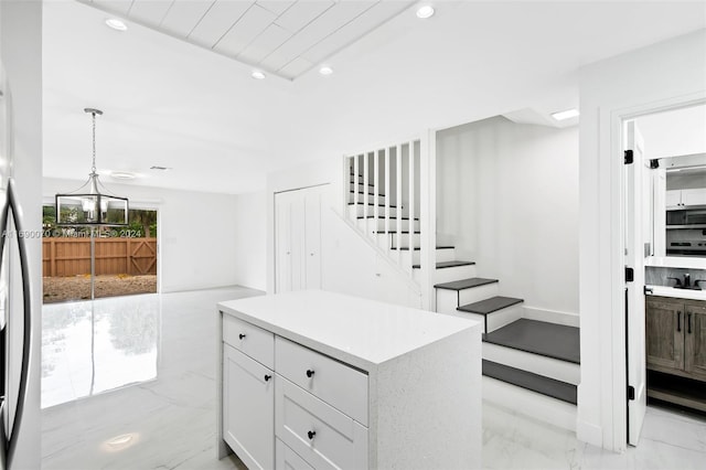 interior space with a center island, white cabinets, a notable chandelier, white fridge, and pendant lighting