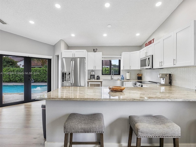 kitchen with white cabinets, vaulted ceiling, light stone counters, and appliances with stainless steel finishes