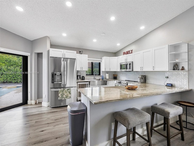 kitchen featuring stainless steel appliances, vaulted ceiling, white cabinets, and kitchen peninsula