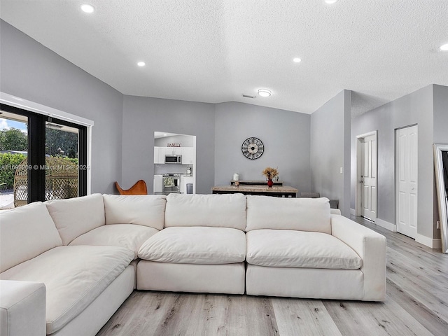 living room with vaulted ceiling, a textured ceiling, light wood-type flooring, and french doors