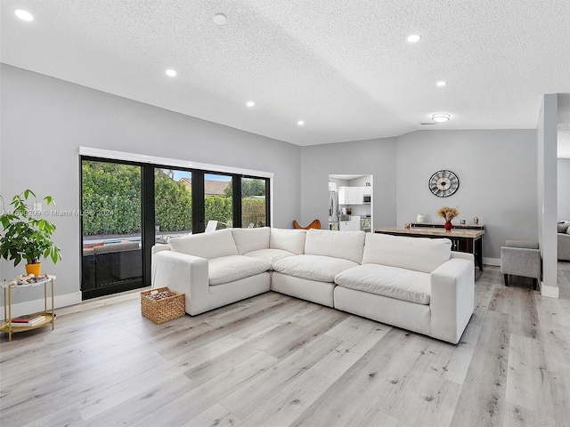 living room with a textured ceiling, light hardwood / wood-style flooring, and lofted ceiling