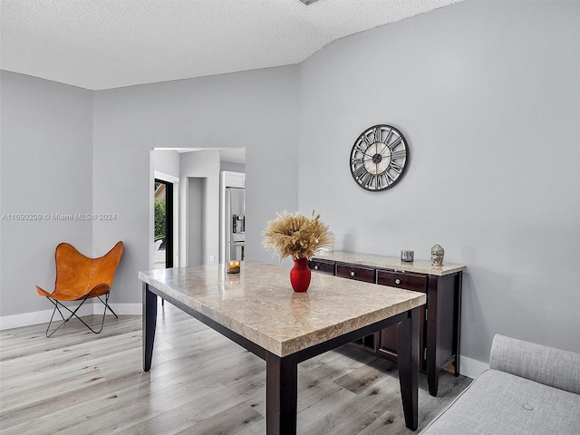 dining room with a textured ceiling, vaulted ceiling, and light hardwood / wood-style flooring