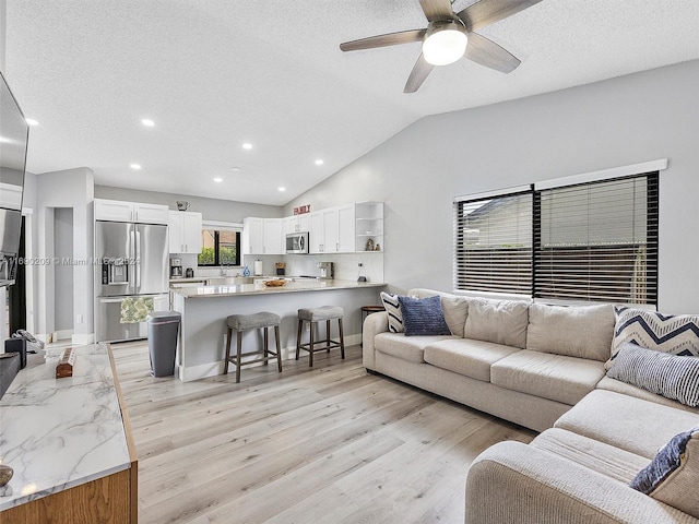 living room with a textured ceiling, light hardwood / wood-style floors, lofted ceiling, and ceiling fan