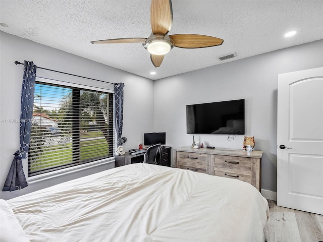 bedroom with ceiling fan, a textured ceiling, and light hardwood / wood-style flooring