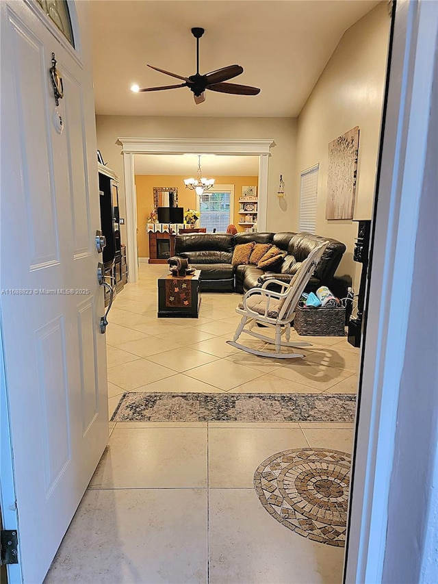 tiled living room with ceiling fan with notable chandelier