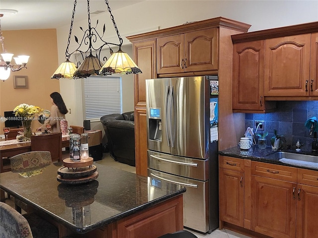 kitchen with sink, dark stone counters, decorative light fixtures, stainless steel fridge with ice dispenser, and decorative backsplash