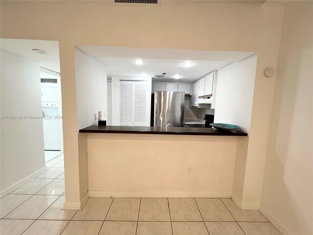 kitchen with stove, white cabinetry, washer / dryer, kitchen peninsula, and stainless steel refrigerator